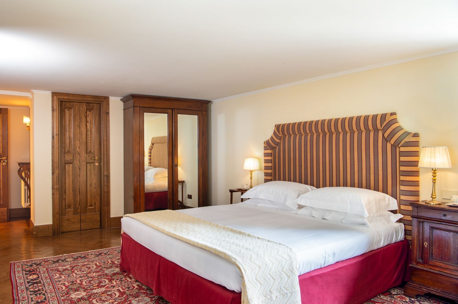 A hotel room with a large bed, wooden wardrobe, and a mirror.