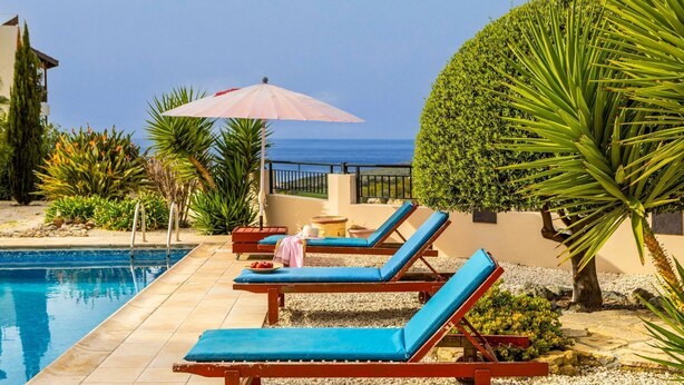 A poolside area with lounge chairs, a table, and a neatly trimmed bush. - Villa Chrysos - Three Bedroom Villa, Sleeps 6 (Tala)