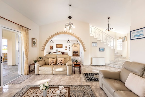 Un salon spacieux avec un canapé beige, une table basse agrémentée d’objets décoratifs, un tapis à motifs et un escalier avec une rampe menant à l’étage supérieur.