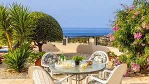 A round glass table with white chairs, a small potted plant, and a tray with food and drinks. - Villa Chrysos - Three Bedroom Villa, Sleeps 6 (Tala)