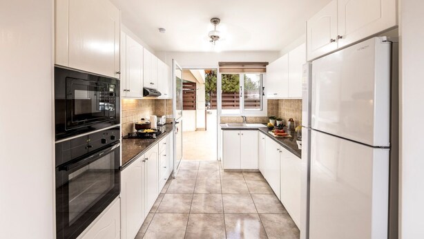 Una cocina moderna con armarios blancos, un horno negro y un refrigerador blanco.
