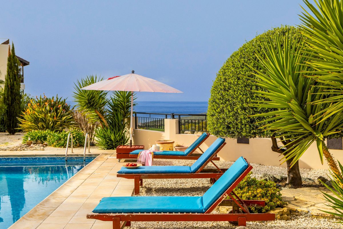 A poolside area with lounge chairs, a table, and a neatly trimmed bush.