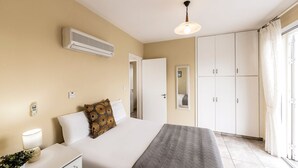 Habitación de hotel con cama, mesita de noche, lámpara, equipo de aire acondicionado, armario y vistas a través de una ventana con cortinas.