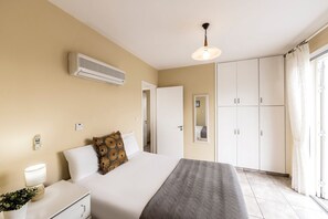 Une chambre d’hôtel comprenant un lit, une table de chevet, une lampe, un climatiseur, une armoire et une fenêtre avec des rideaux, offrant une vue sur l’extérieur.