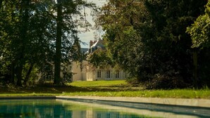 Una piscina con una casa al fondo, rodeada de árboles.