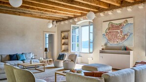 A spacious living room with a wooden ceiling, a large window, and a map on the wall. - Villa Reverie - Seven Bedroom Villa, Sleeps 14 (Sudurad)