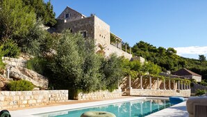 A pool area with lounge chairs, a stone wall, and a building with a stone facade. - Villa Reverie - Seven Bedroom Villa, Sleeps 14 (Sudurad)