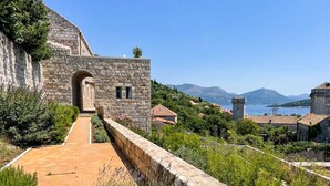 A stone building with an arched entrance, a paved pathway, and a view of the sea and mountains in the background. - Villa Reverie - Seven Bedroom Villa, Sleeps 14 (Sudurad)