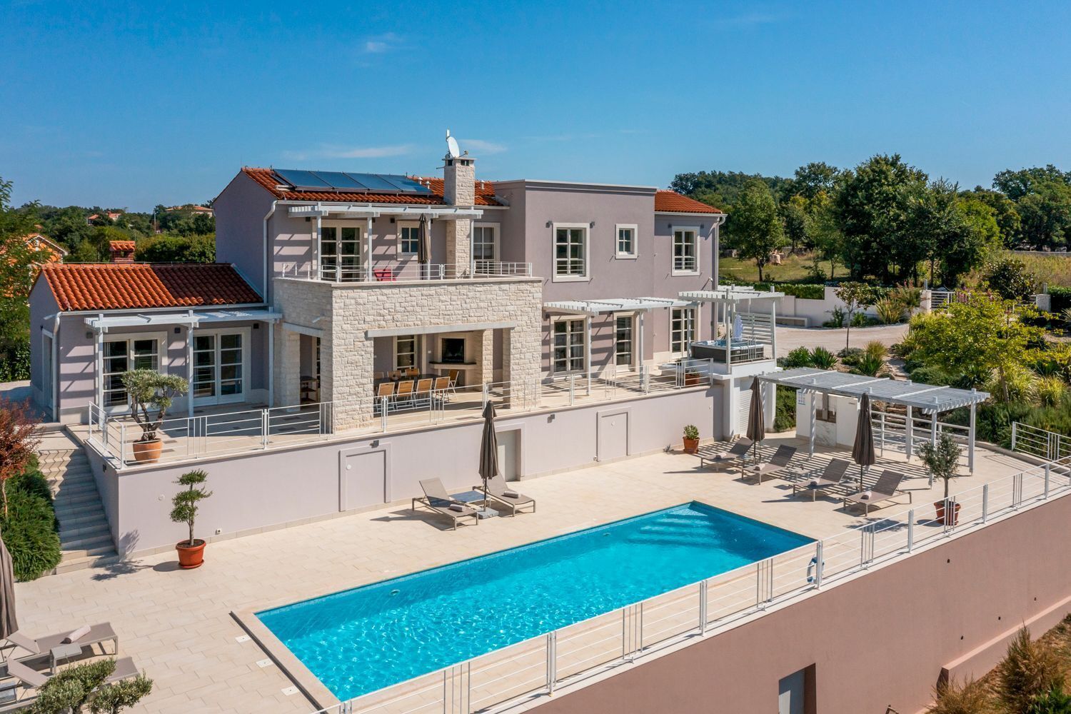 A two-story house with a swimming pool, outdoor seating, and a stone facade.