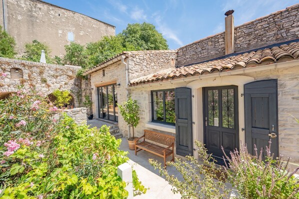 A stone building with a tiled roof, a bench, and a small garden area with various plants.
