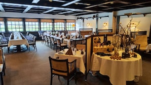 A restaurant with long communal tables, individual tables with centerpieces, and a view of a garden through large windows. - Banegaardshotellet (Vojens)