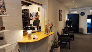 A reception area with a wooden desk, a black lamp, a computer, and a wall-mounted clock. - Banegaardshotellet (Vojens)
