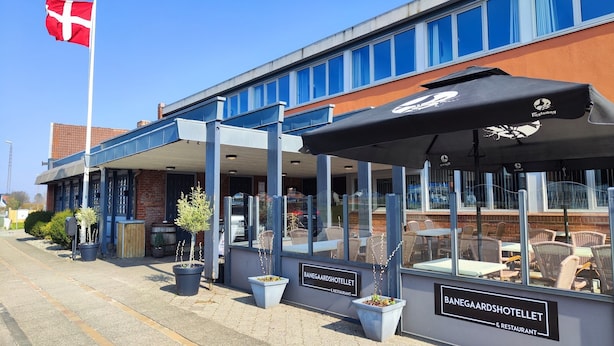 A hotel with outdoor seating, a flag, and a sign reading "BANEGAARDSHOTELLET & RESTAURANT". - Banegaardshotellet (Vojens)