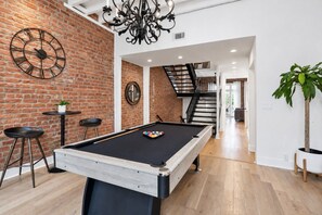 A pool table in a room with a brick wall, a clock, and a staircase. - Renovated Arts District Townhouse Steps to FQ (New Orleans)