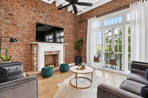 A room with a brick wall, a fireplace, a ceiling fan, and a large window with a view. - Renovated Arts District Townhouse Steps to FQ (New Orleans)