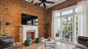 A spacious living room with a brick wall, a fireplace, and a large window with curtains.