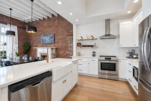 Una cocina moderna con pared de ladrillo, muebles blancos, electrodomésticos de acero inoxidable e iluminación colgante.