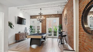 A modern living room with a pool table, a TV mounted on the wall, and a brick wall with a circular mirror.