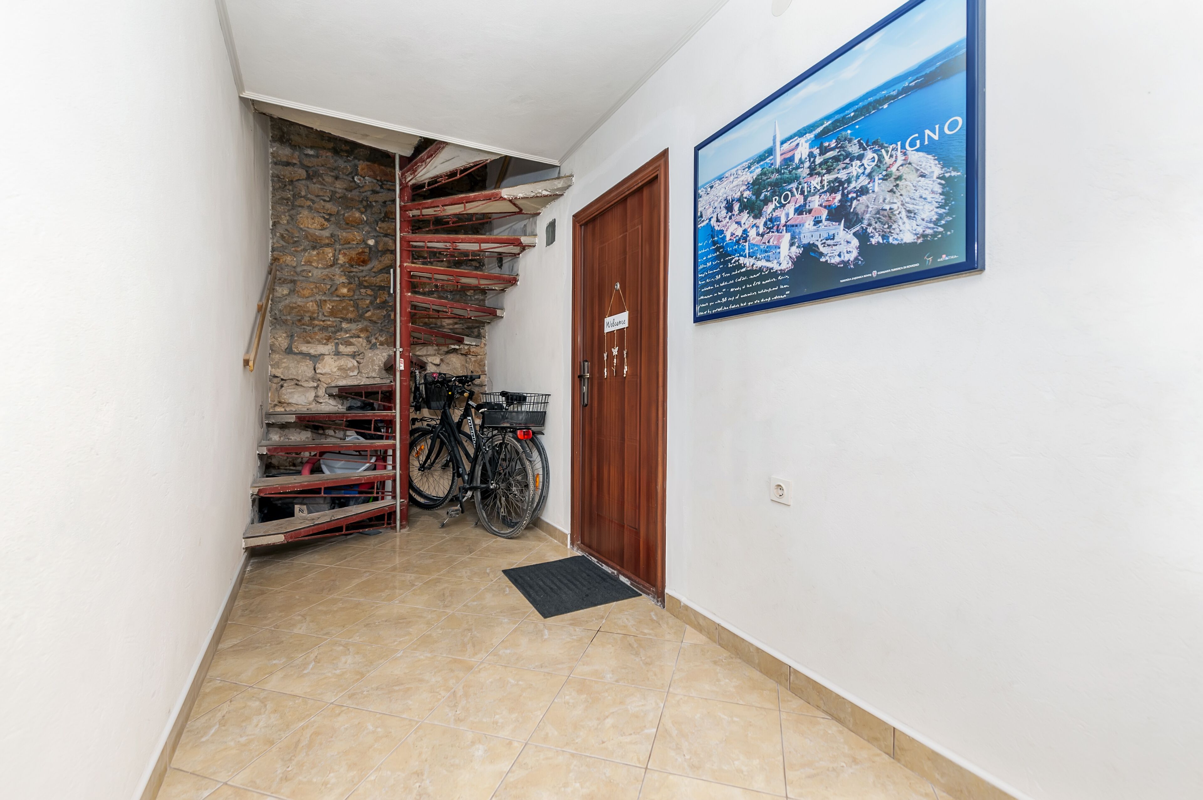 Un pasillo estrecho con una escalera de piedra, una puerta de madera y una bicicleta.