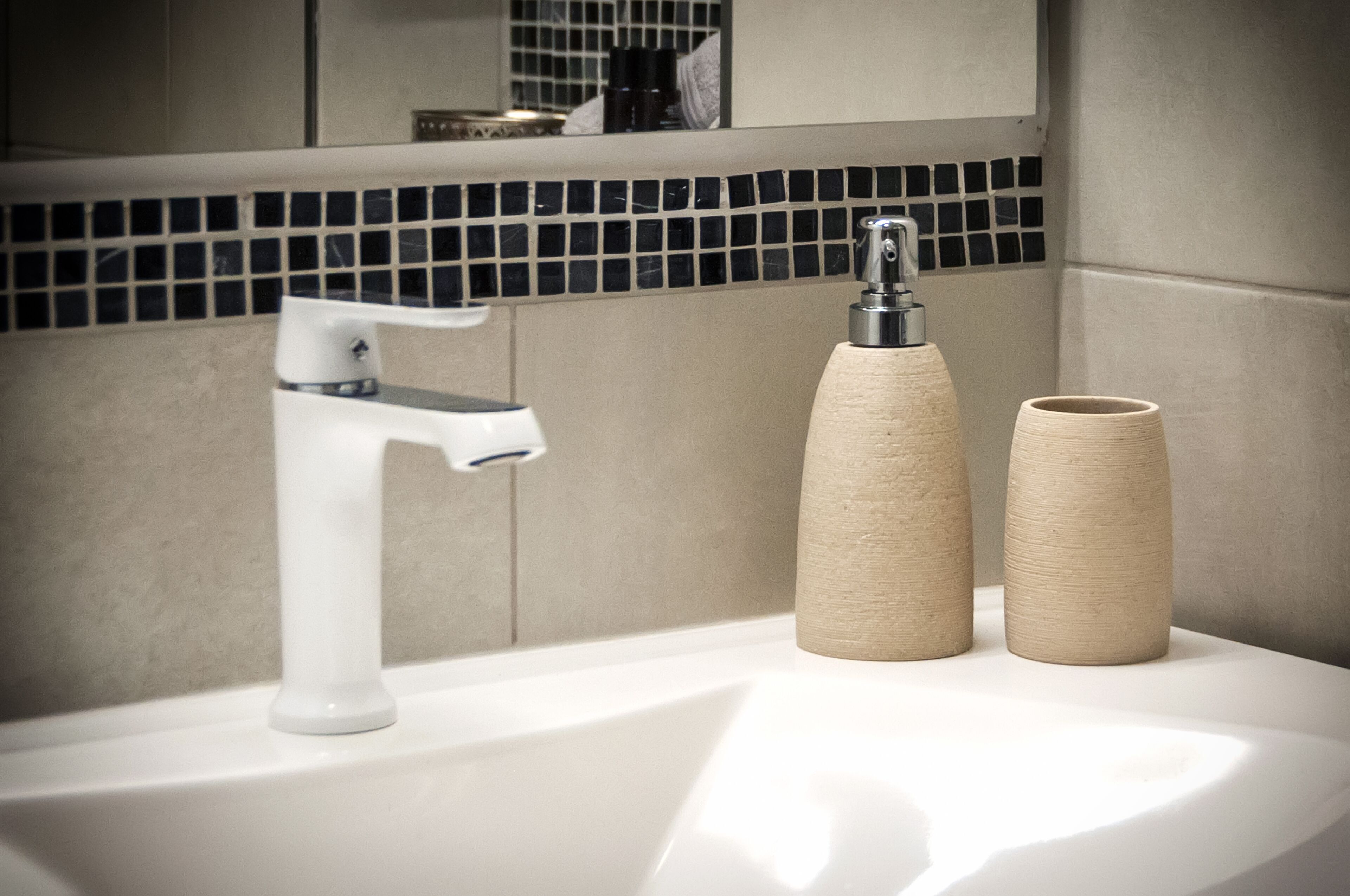 A bathroom sink with a modern faucet and two cylindrical containers on the counter.