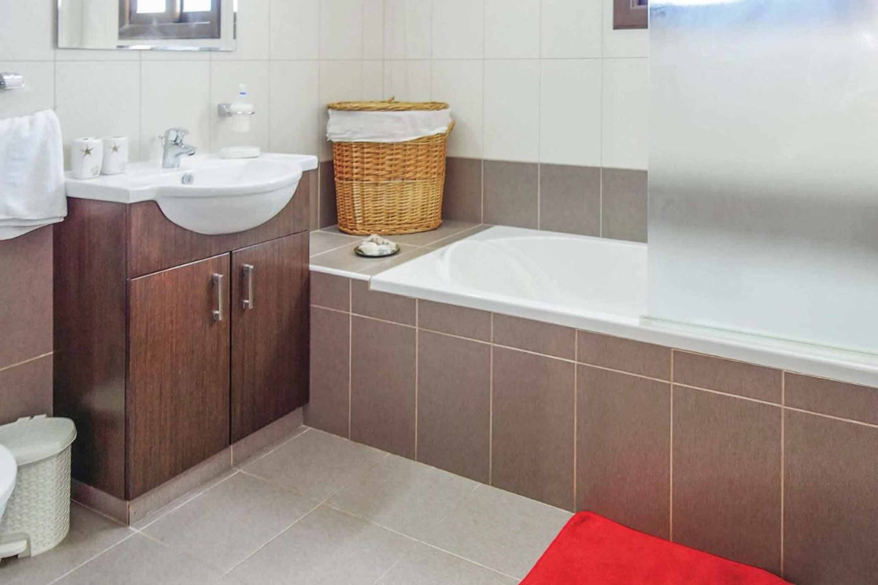 A modern bathroom with a white sink, dark wooden cabinets, a large bathtub, and a wicker basket.