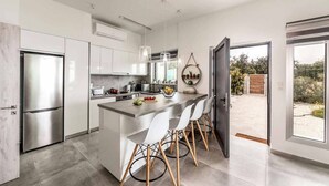 A modern kitchen with a central island, stainless steel appliances, and a view to the outdoors. - Latchi Infinity Blue (Neo Chorio)