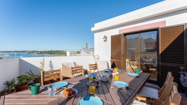 A wooden table set for breakfast with a view of the sea and a lighthouse in the background.