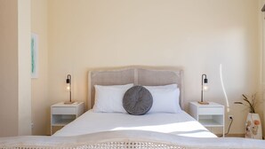 A neatly made bed with a rattan headboard, two bedside tables with lamps, and a wall-mounted shelf.