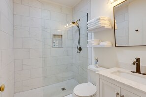A modern bathroom with a glass-enclosed shower, white marble tiles, a white toilet, and a vanity with a mirror and towel rack. - Extended Stays Welcome! Home 1 Block to Avondale (Birmingham)
