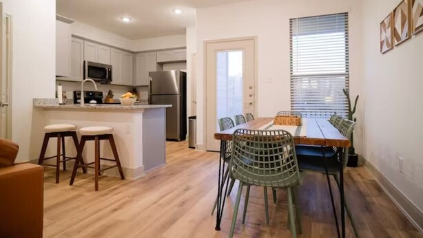Une cuisine moderne avec des meubles blancs, un réfrigérateur en acier inoxydable et un four à micro-ondes. On y trouve également un coin repas avec une table en bois et des chaises vertes.