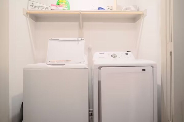 A laundry area with two white washing machines, a shelf with a detergent box, and a small item on the shelf. - Quality furnished home existing to serve our guest (San Antonio)