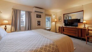 A hotel room with a large bed, a TV, a dresser, and a desk with a lamp. - 1BR Waterfront Condo in Downtown BH [Ocean Breeze] (Bar Harbor)