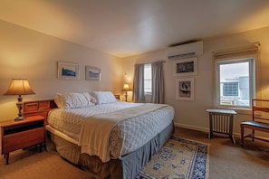 Une chambre à coucher comprenant un lit, des tables de chevet, une chaise, une fenêtre avec des rideaux et des œuvres d’art murales.