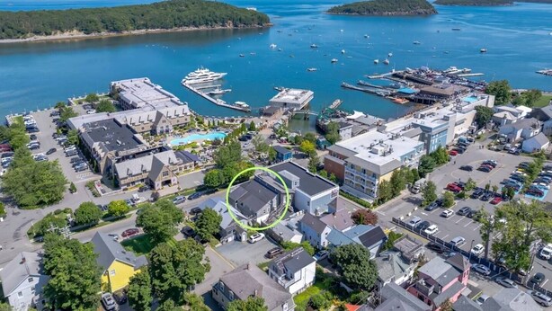 An aerial view of a coastal town with a marina, residential buildings, and a large hotel with a swimming pool. - 1BR Waterfront Condo in Downtown BH [Ocean Breeze] (Bar Harbor)