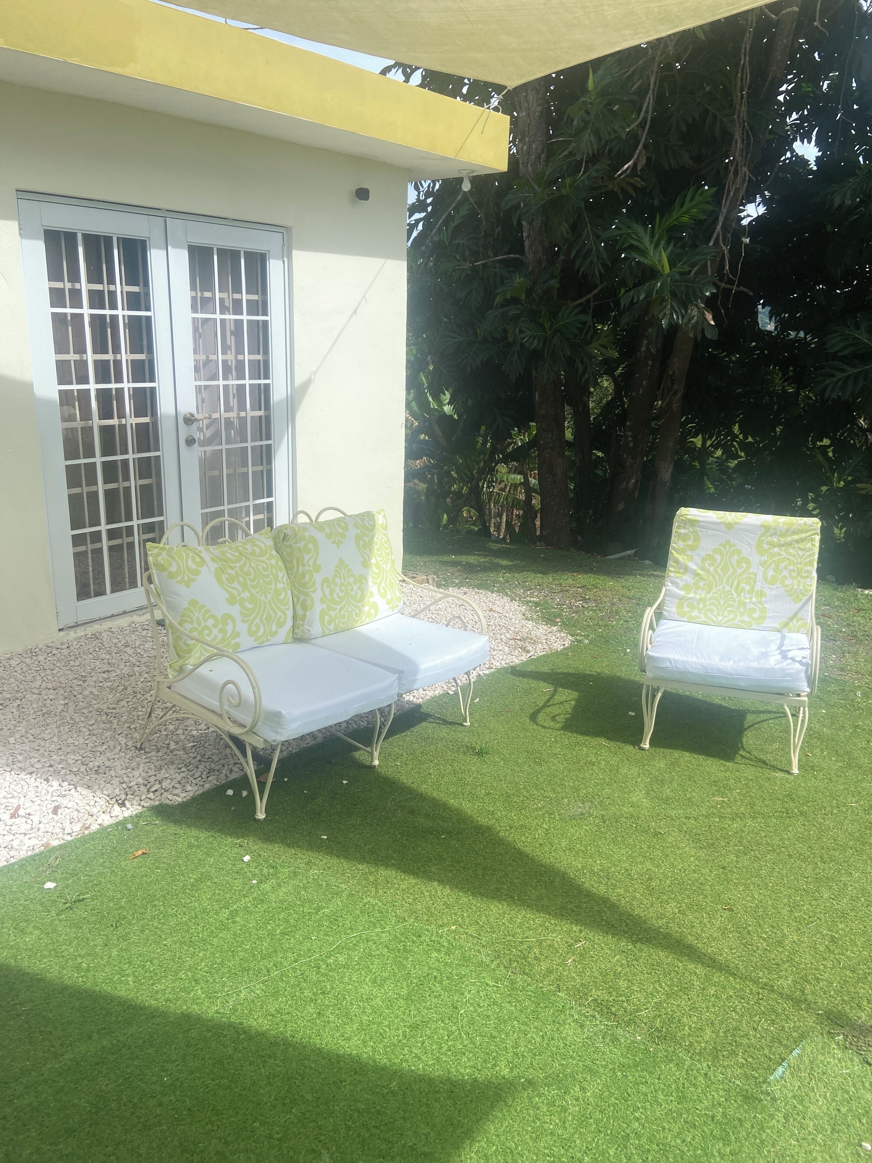 Un patio con dos sillas de metal blanco y un sofá de metal blanco con cojines estampados verdes.