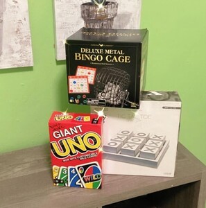 Ein Tisch mit einem großen UNO-Kartonsatz, einem Deluxe-Metall-Bingo-Käfig und Tic Tac Toe Karten.