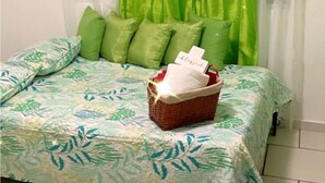 A bed with a floral-patterned bedspread, green pillows, and a basket with a white towel.
