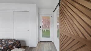A bedroom with a bed, a door with a frosted glass panel, and a wooden wall. -  NEW Build-777 Hideaway (Grants Pass)