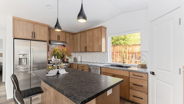 A modern kitchen with wooden cabinets, a stainless steel refrigerator, a granite countertop, and pendant lighting. -  NEW Build-777 Hideaway (Grants Pass)