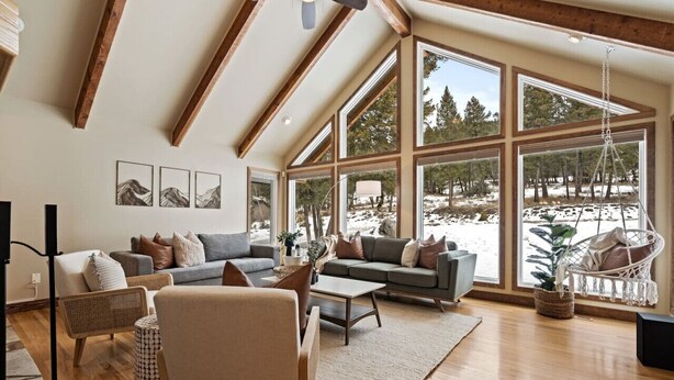 A spacious living room with a high ceiling, large windows, and a view of a snowy landscape.