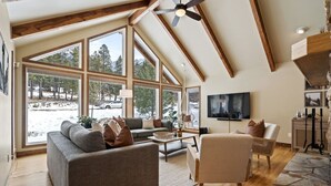 A spacious living room with large windows, a fireplace, and a ceiling fan.