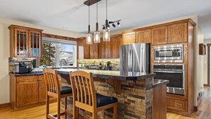 A kitchen with wooden cabinets, a stone island, stainless steel appliances, and hanging pendant lights.