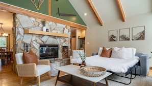 A cozy living room with a stone fireplace, a sofa, a coffee table, and a dining area with wooden furniture.