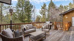 A wooden deck with wicker furniture, a grill, and a view of trees.