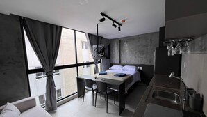 A modern hotel room with a bed, a desk, a chair, a sofa, and a kitchen area. - Flat Premium Ozean Home & Service - João Pessoa (João Pessoa)