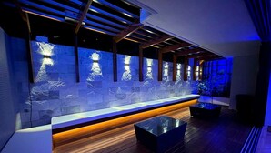 A modern bar area with a stone wall, wooden bench, and a glass-top table. - Flat Premium Ozean Home & Service - João Pessoa (João Pessoa)