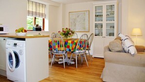 Une cuisine compacte comprenant un lave-linge, une table à manger avec des chaises, un meuble avec des portes en verre et un canapé.