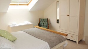 Une chambre avec un puits de lumière, un lit avec un oreiller vert, une chaise et une armoire.