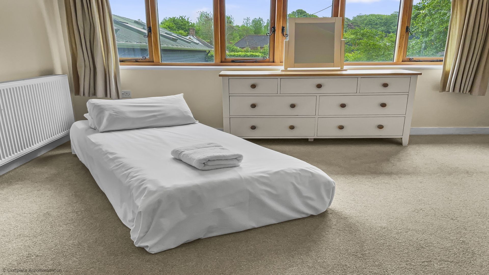A bedroom with a bed, a dresser, and a window with a view of greenery.