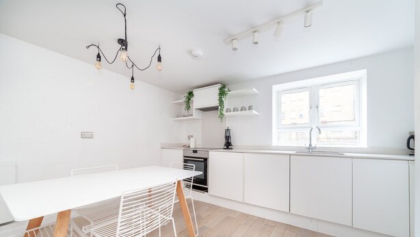 A modern kitchen with white cabinetry, a dining table with metal chairs, and a window providing natural light.